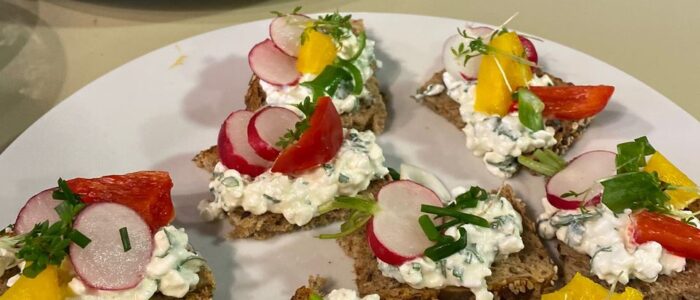 Auf Tellern angerichtetes geschnittene Brotscheiben mit Kräuterquark und geschnittenem Gemüse.