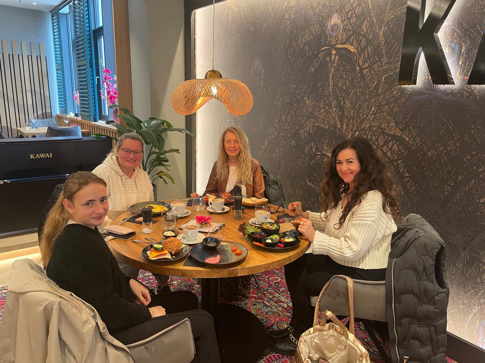 Julia, Mama Natalie, Sabine, ehrenamtliche des inklusiven Broadwood Projektes und Anne Meier als Modeberaterin sitzen um einen Frühstückstisch in einem Restaurant.
