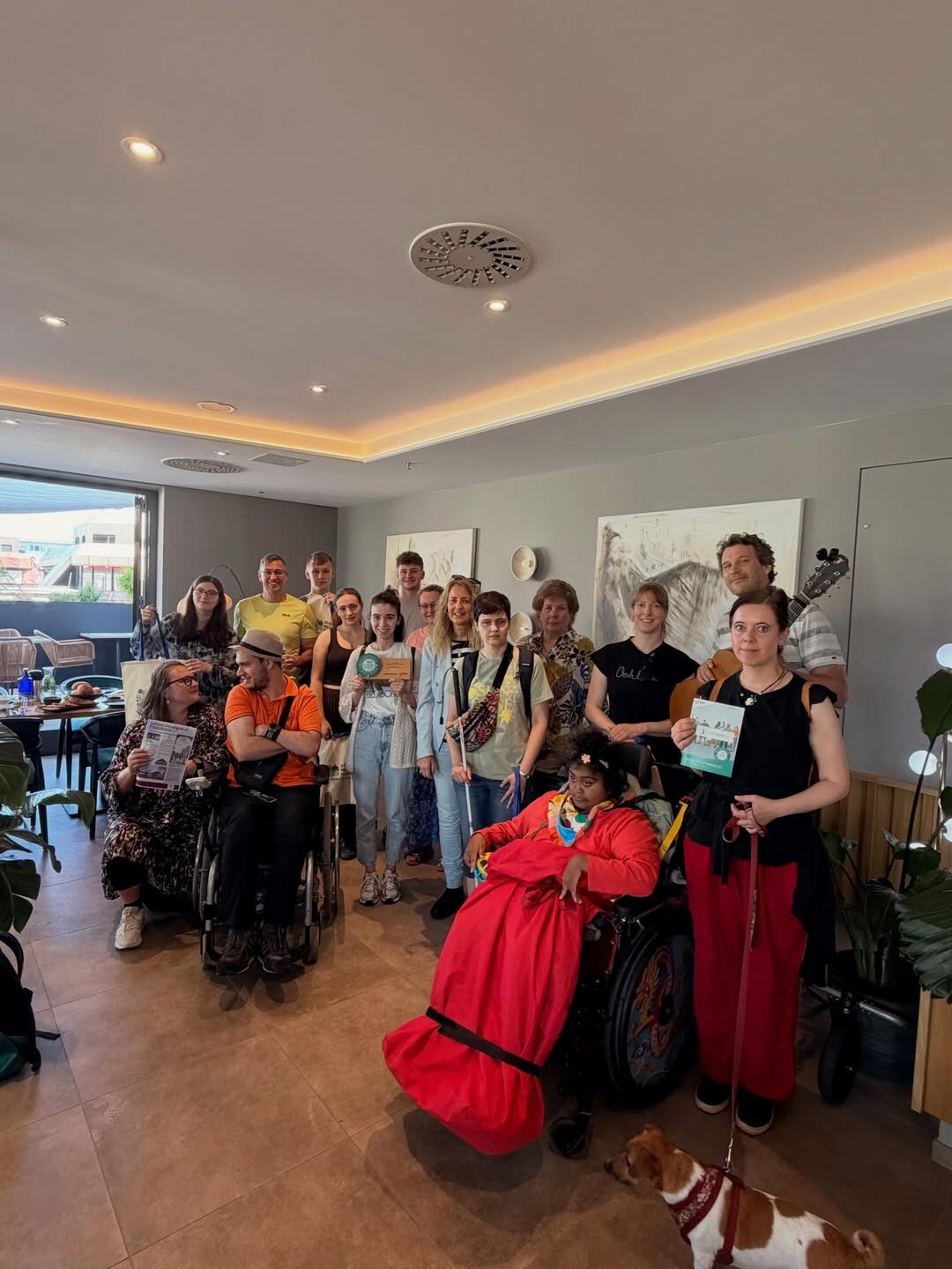 Eine Gruppe von Menschen steht und sitzt gemeinsam im Kawaii Restaurant in Paderborn. Einige Personen nutzen einen Rollstuhl. Die Gruppe macht ein Erinnerungsfoto. In der Gruppe sind auch Kinderbuchautorin Maren Graf und Musiker Matthias Lüke.