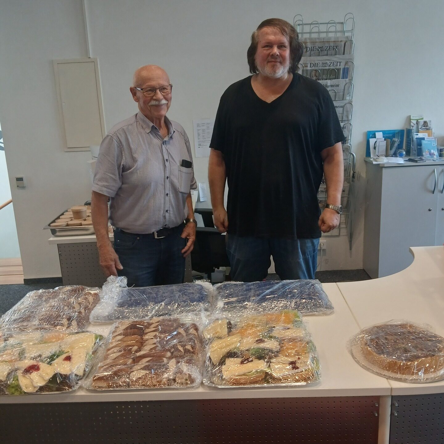 Lars Hesse und sein Vater Manfred Hesse stehen hinter einem Essenbuffet mit abgedeckten Speisen.